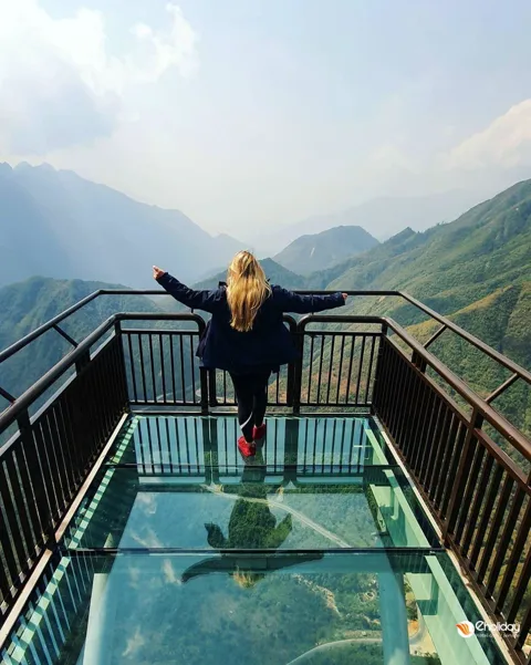Sapa Glass Bridge extending over a mountain pass with clouds and distant peaks