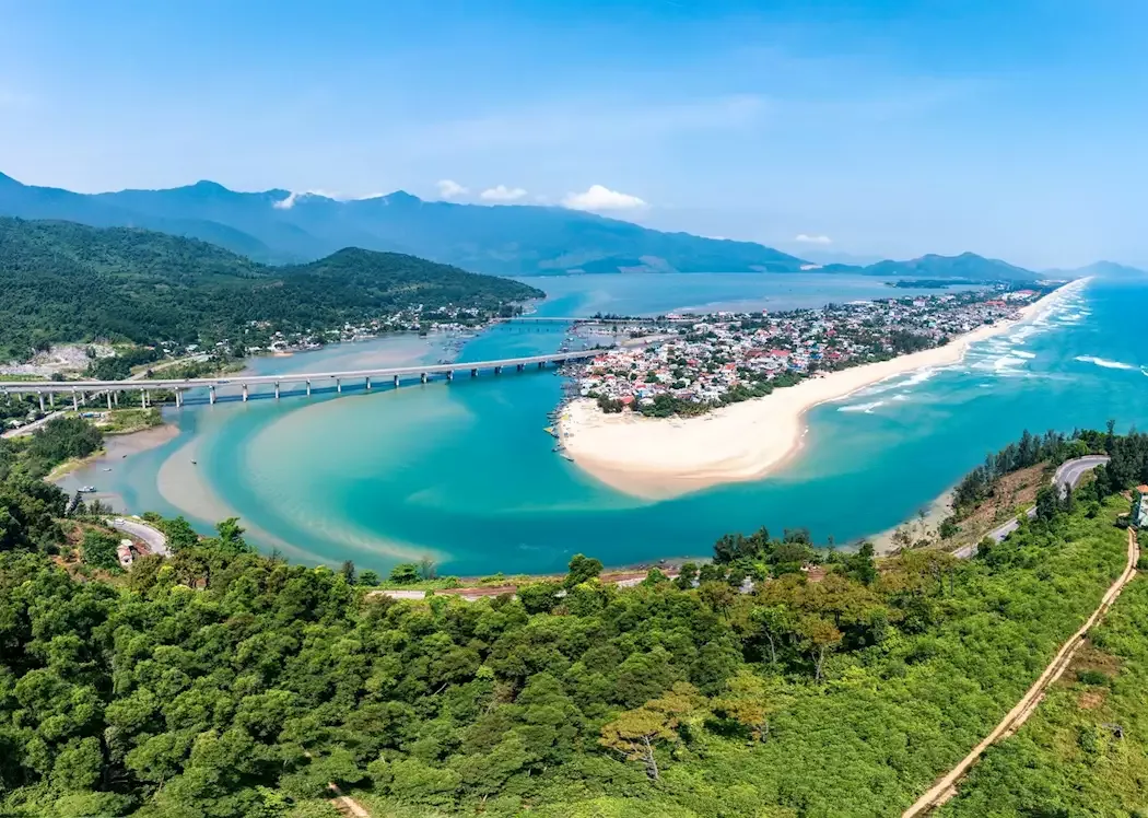 Panoramic view of Lang Co Beach with white sand, clear turquoise water, lush green mountains, and Lap An Lagoon in Central Vi