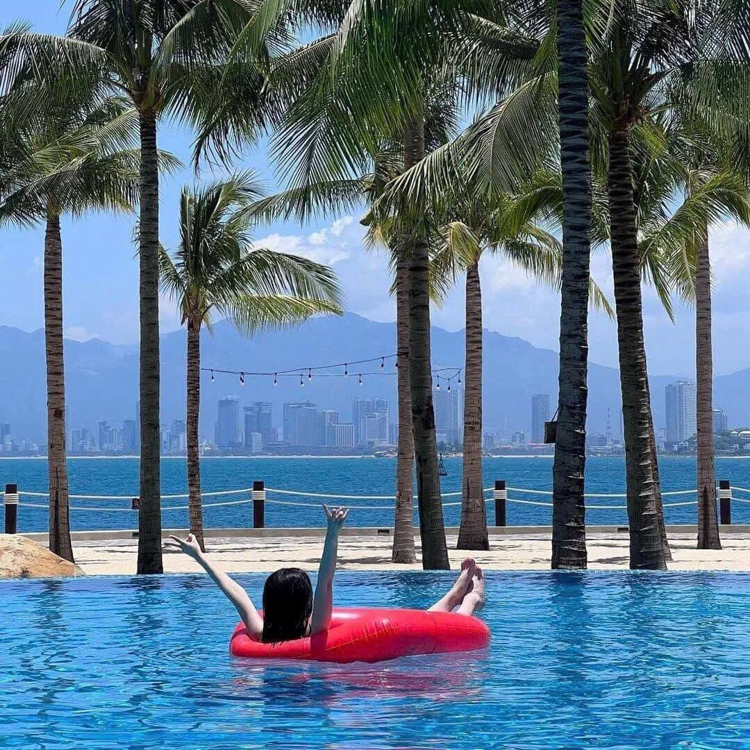 Panoramic view of Nha Trang beach with clear blue water, white sand, lush green mountains, and boats in the bay