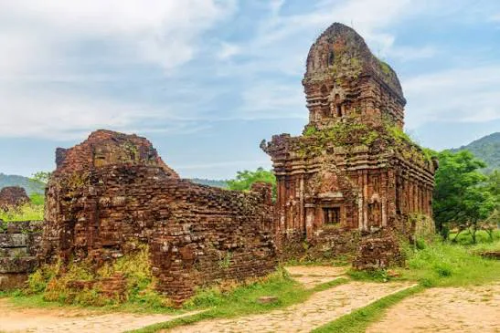 Ancient Cham temples at My Son Sanctuary, Central Vietnam, surrounded by lush green jungle and mountains under a clear sky.