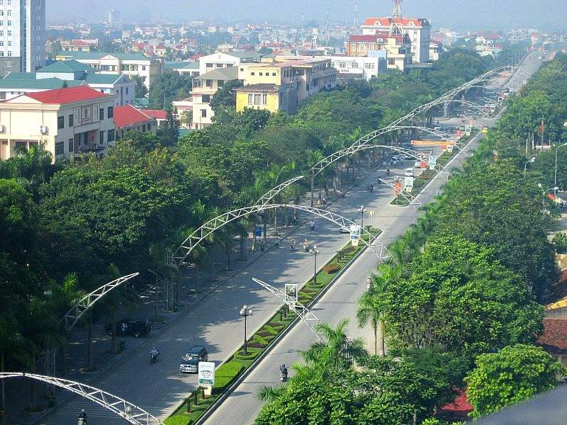 Panoramic view of Thanh Hoa City with modern buildings, a river, and distant green hills under a clear sky, showcasing urban