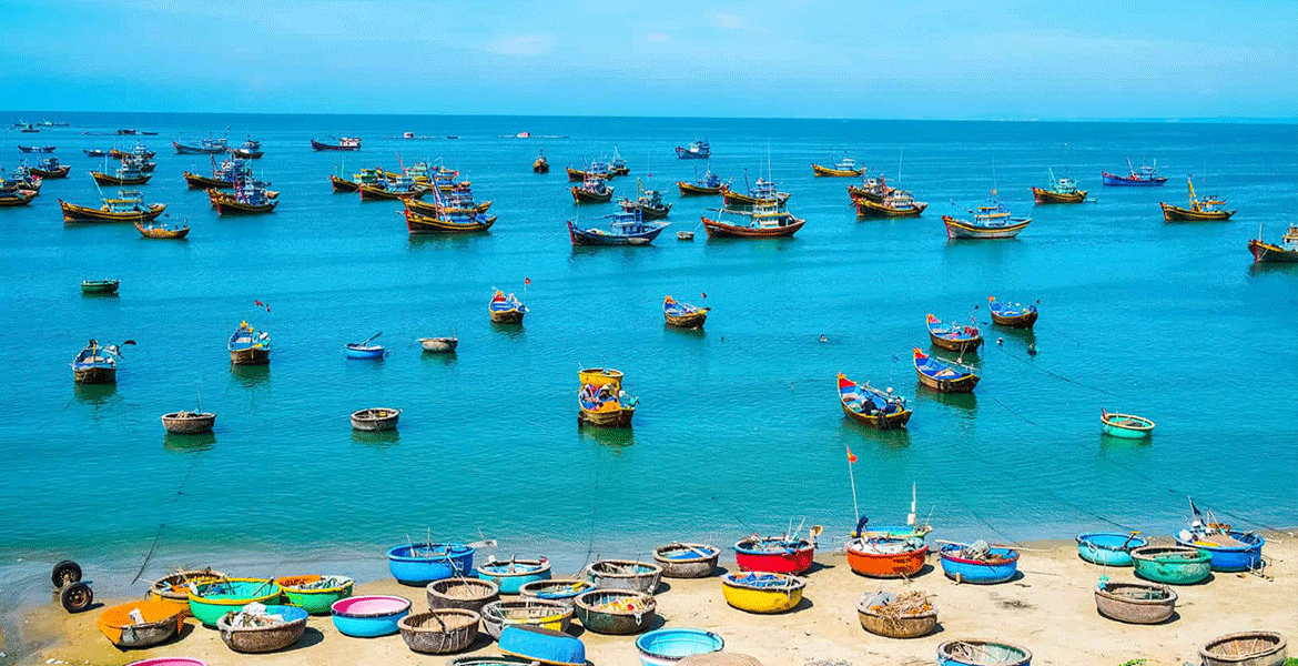 Panoramic view of Mui Ne's iconic Red Sand Dunes at sunset with tourists sandboarding and a traditional fishing boat in the d