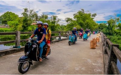 Vespa scooter parked near a traditional tile-roofed bridge in Hue countryside